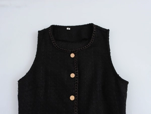 Dettaglio di abito in tweed nero con catena dorata e bottoni metallici sulla scollatura