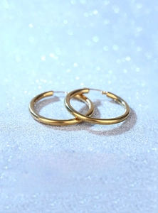 Polished gold hollow hoop earrings shown against a dreamy blue bokeh background