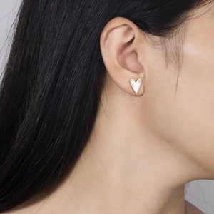 Close-up of white heart earring with gold border worn by a model in soft lighting