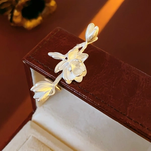 Macro shot of silver metal magnolia flower branch jewelry on a brown leather box
