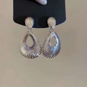 Elegant silver teardrop earrings with textured shell pattern on a black display card