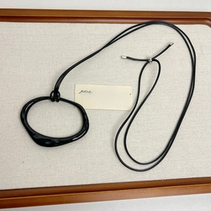 Close-up of minimalist black irregular pendant on leather cord in a wooden jewelry tray