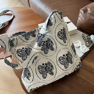 Detailed texture of beige canvas tote bag with artistic butterfly embroidery on a sofa