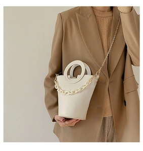 Detail of off-white leather bucket bag featuring round handle and decorative chunky chain