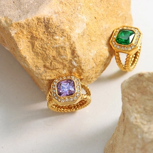 Golden titanium steel rings with purple and green square stones on a natural rock