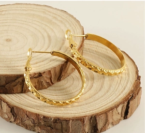 Macro view of gold plated hoop earrings with hammered texture on natural wood backdrop