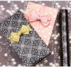 Detail of pink and black gift boxes with geometric gold foil patterns and satin ribbons