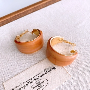 Vue à plat de boucles d'oreilles créoles C en résine ambrée sur tissu texturé