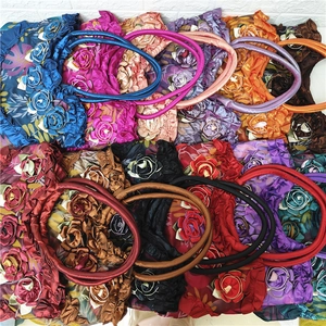 Detailed stack of satin shoulder bags with 3D roses and ruffled edges in various colors