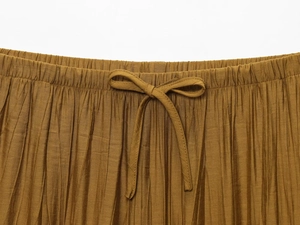 Detail of ochre pleated fabric showing elastic waistband and drawstring bow tie