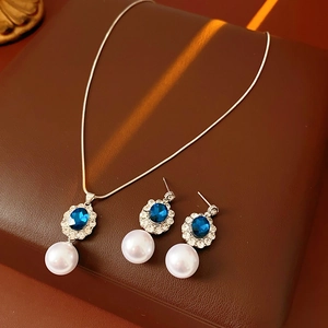 Dettaglio di parure vintage con gemme blu e perle bianche su sfondo strutturato marrone