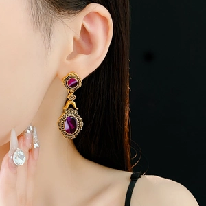 Close-up of vintage gold floral earrings with purple oval gems on a model