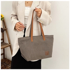 Detail of grey canvas tote bag with leather logo and brown handles worn by a model