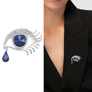Evil eye brooch with blue crystal teardrop shown on white background and black blazer