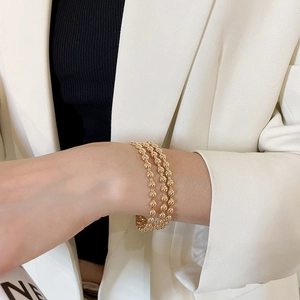 Detail of a three-layer gold beaded cuff bracelet worn on a wrist with minimalist style