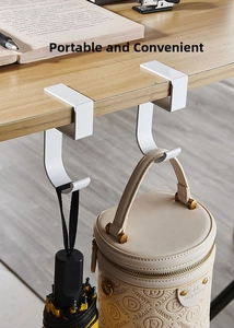 Close-up of portable white metal desk hooks holding bags on a wooden table edge