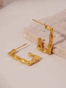 Macro detail of gold bamboo texture U-shaped geometric earrings on a stone base