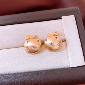Macro detail of apple-shaped gold earrings with brushed metal finish and tiny zircons