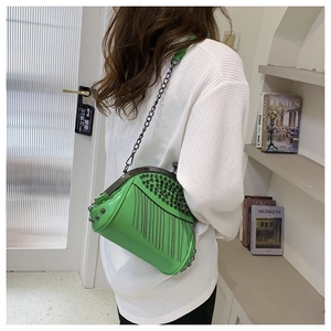 Detail of green punk crossbody bag featuring metal studs and silver chain tassels