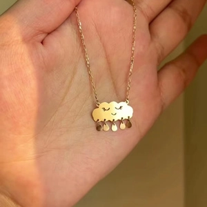 Détail d'un collier pendentif nuage doré avec visage souriant et gouttes de pluie suspendues