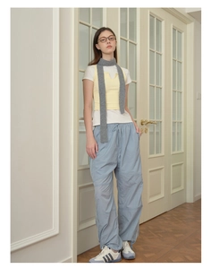 Detail showing a grey narrow knit scarf paired with a casual yellow vest and blue pants