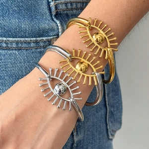 Détail de bracelets œil protecteur dorés et argentés avec cils sur fond en jean bleu