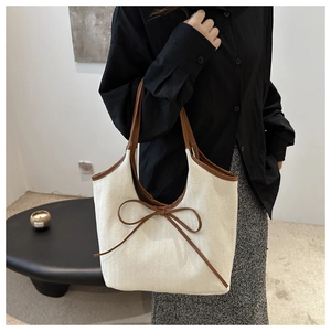 Detail of canvas tote bag with brown leather trim and decorative bow on the side