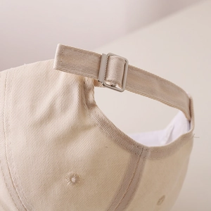 Dettaglio del cappellino in cotone beige con fibbia in metallo regolabile sul retro