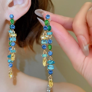 Detailed close-up of long drop earrings with colorful rhinestones in a gold metal setting