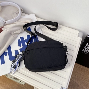 Close-up of black nylon crossbody bag with adjustable strap and floral charm on a suitcase