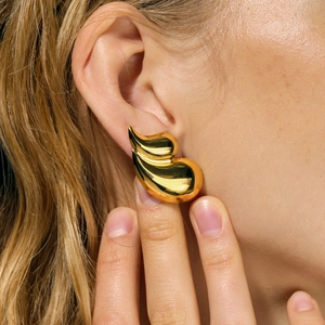 Close-up of a large gold polished organic leaf-shaped earring on a model ear