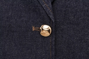Macro detail of a vintage gold organic button on dark blue denim fabric with stitching