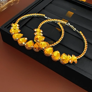 Detailed close-up of large round drop earrings with yellow crystals on black leather