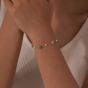 Detail of a gold bracelet featuring green gemstone beads and small white pearls on a wrist