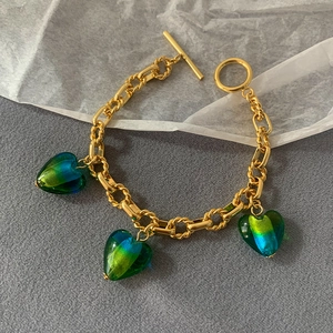 Detail of gold-plated bracelet featuring green-blue gradient glass heart pendants and T-bar clasp