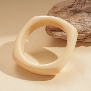 Detail of a chunky square cream resin bangle resting on a natural textured stone