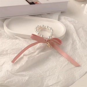 Detail of white pearl hair tie with pink silk bow and heart pendant on white tray