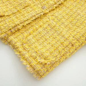 Detail of yellow tweed fabric texture with fringe edges and a gold decorative button