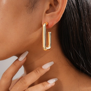 Close-up of a minimalist gold rectangular metal earring worn by a model in soft light