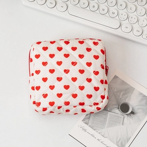Flat lay of a white quilted makeup bag with red heart pattern and a red zipper