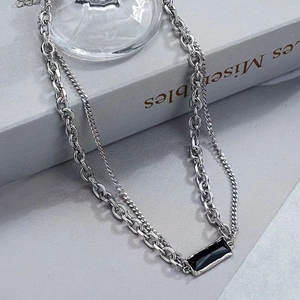 Detail of a layered silver necklace featuring a sleek black rectangular stone pendant