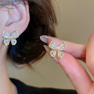 Close-up of gold butterfly stud earrings with white zircons and a central pearl