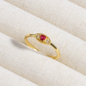 Macro shot of gold ring with oval red gemstone and white zircon accents on fabric