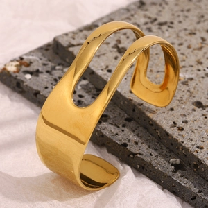 Detail of 18K gold-plated asymmetrical wide hollow wave bangle on dark textured stone