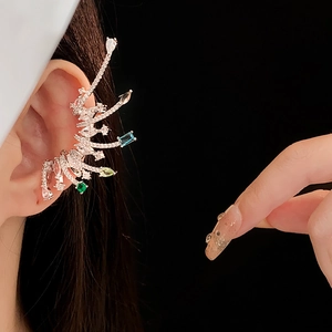 Close-up of a silver wing-shaped ear cuff with blue and green gems on a black background