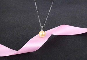 Macro shot of gold pearl pendant on silver chain with pink ribbon on dark background