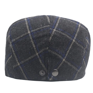 Macro detail of navy and grey plaid wool newsboy cap showing metal buckle and fabric texture