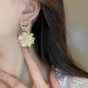 Détail de boucles d'oreilles fleurs en acrylique crème et clous dorés sur modèle