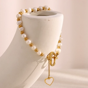 Detail of 18K gold plated bead and pearl bracelet with heart clasp on ceramic