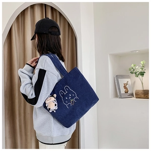 Dark blue corduroy tote bag with rabbit embroidery and cow plush charm shown on model